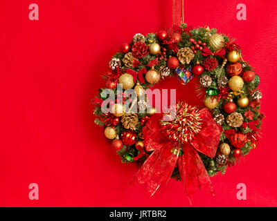 A Christmas Wreath. mit Bällen, Bändern verziert, Tannenzapfen, Muscheln und Glocken hängt auf rotem Hintergrund. Stockfoto