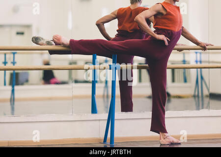 Tanz, Kleidung, Schönheit Konzept. harte Ballett Tänzerin tragen Gemütliche sweatpants in kastanienbraunen Farbe und Karotte-rot ärmelloses top Übungen in Dance Hall in der Nähe choreografische Maschine Stockfoto