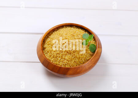 Schüssel mit trockenen Weizen Bulgur auf weißem Holz- Hintergrund Stockfoto