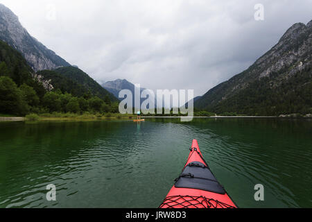 Foto einer Frau in Shorts Stand up Paddeln auf alpinen See, takoen von Kajak. Lago di Predil, Italien. Stockfoto