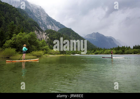 Mutter und Sohn in einen Taucheranzug paddeln auf dem Zusatzsteuerventil-Armaturenbrett (SUP) auf alpinen See, Lago di Predil, Italien. Stockfoto