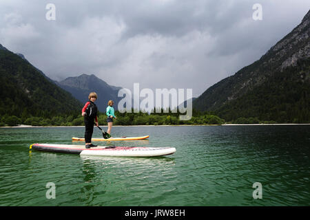 Mutter und Sohn in einen Taucheranzug paddeln auf dem Zusatzsteuerventil-Armaturenbrett (SUP) auf alpinen See, Lago di Predil, Italien. Stockfoto