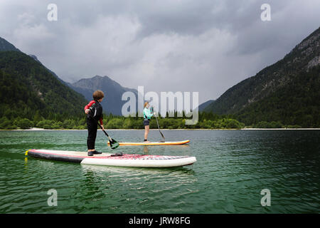 Mutter und Sohn in einen Taucheranzug paddeln auf dem Zusatzsteuerventil-Armaturenbrett (SUP) auf alpinen See, Lago di Predil, Italien. Stockfoto