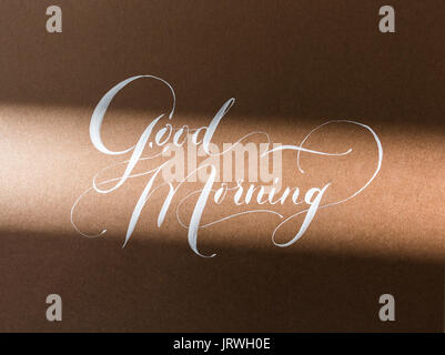 Kunst, Leidenschaft, Kalligraphie Konzept. Auf dem Papier der Schokolade Farbe gibt es Grußworte guten Morgen mit weißer Tinte in schönen chic Roundhand Script mit verschiedenen ornamentalen Verzierungen geschrieben Stockfoto