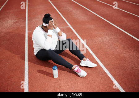 Frustrierte übergewichtige Frau in Sportswear sitzen auf Laufbahn Stockfoto