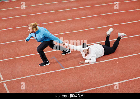 Personal Trainer ziehen erschöpft übergewichtige Frau auf Track bestimmt Stockfoto