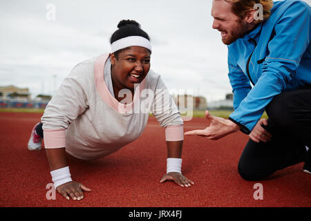 Fette Frau tun Push-ups motiviert durch persönliche Trainer Stockfoto