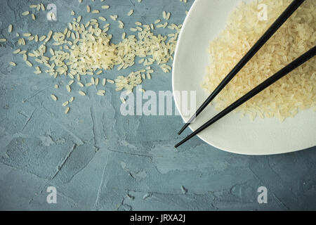 Porzellanteller und Reis auf grauem Beton Tabelle mit Copyspace Stockfoto