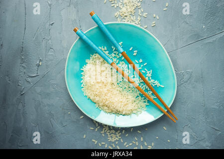 Porzellanteller und Reis auf grauem Beton Tabelle mit Copyspace Stockfoto