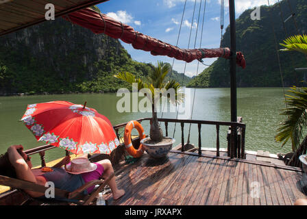 Touristen entspannen im Inneren einer chinesischen Dschunke, Halong Bay Tourist Boat tour, Vietnam. Junk, Boot segeln unter karst Kalkstein Berge auf Cat ba nationa Stockfoto