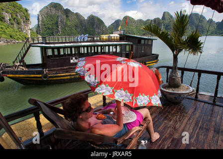 Touristen entspannen im Inneren einer chinesischen Dschunke, Halong Bay Tourist Boat tour, Vietnam. Junk, Boot segeln unter karst Kalkstein Berge auf Cat ba nationa Stockfoto
