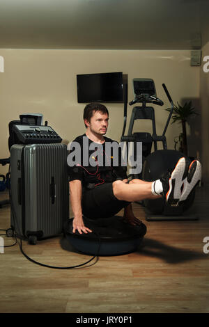 Fitness athletische Mann in elektrischen muskuläre Stimulation Anzug tun L-Sit plank auf bosu Ball in der Turnhalle Stockfoto