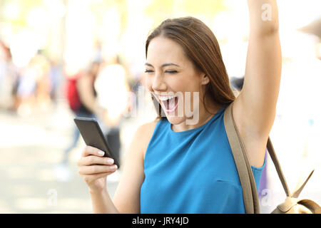 Aufgeregt Frau heben den Arm erhalten gute Nachrichten auf ein Handy auf der Straße Stockfoto