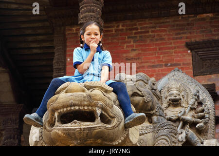 Junge nepalesische Mädchen sitzen auf die Statue eines Löwen in Bhaktapur. Stockfoto