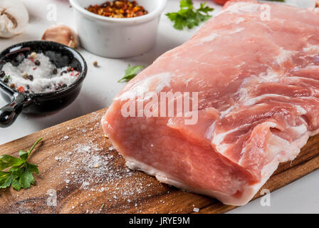 Rohes Fleisch mit Zutaten für das Abendessen. Schweinefilet, Filet, auf ein Schneidbrett, mit Salz, Pfeffer, Petersilie, Rosmarin, Öl, Knoblauch, Tomaten, Pilze. B Stockfoto