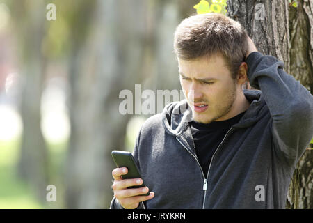 Verwirrt single Teen Reading eine Nachricht in einem Smart Phone im Freien in einem Park Stockfoto