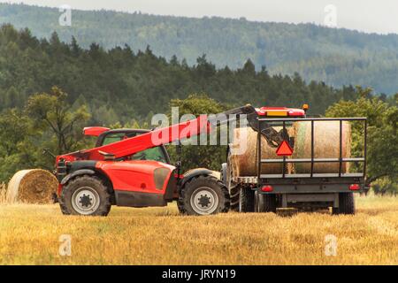 Ausziehbare Sammler Sammler Stroh auf dem Feld in der Tschechischen Republik. Arbeit in einem landwirtschaftlichen Betrieb. Sammeln von Strohballen Stockfoto