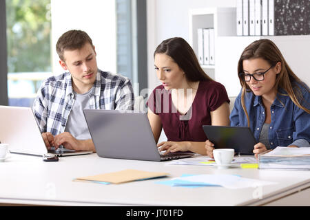 Drei aufmerksame Mitarbeiter auf Linie gemeinsam mit mehreren Geräten im Büro Stockfoto