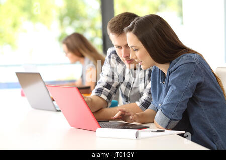 Zwei konzentrierte Studenten arbeiten zusammen auf der Linie mit einem Laptop in einem Klassenzimmer Stockfoto