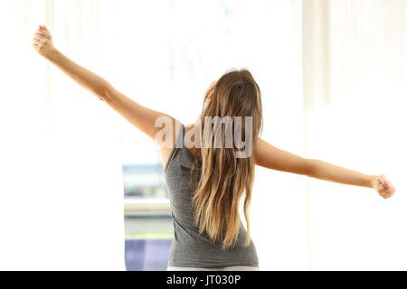 Rückansicht eines Mädchens stretching Arme aufwachen Blick durch das Fenster in der Früh zu Hause. Stockfoto