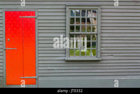 Helle rote Tür in Braun Wand von Gebäude aus der Kolonialzeit mit multipaned Fenster Stockfoto