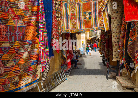 Das Leben auf der Straße. Teppiche mit traditionellen Mustern zum Verkauf zu einem souq, Markt, Basar. Souk Medina von Fes, Fes el Bali. Marokko, Maghreb Nordafrika Stockfoto