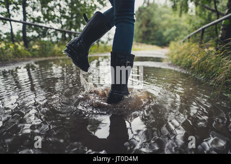 In der Nähe der Beine junge Frau mit Gummistiefeln springen und tanzen in einer Pfütze Stockfoto