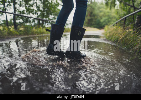 In der Nähe der Beine junge Frau mit Gummistiefeln springen und tanzen in einer Pfütze Stockfoto