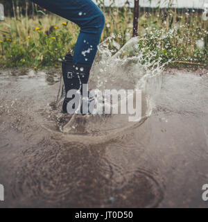 In der Nähe der Beine junge Frau mit Gummistiefeln springen und tanzen in einer Pfütze Stockfoto