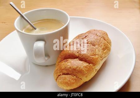 Frühstück mit Kaffee und frischen Croissant auf einem weißen Teller. Stockfoto