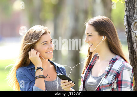 Zwei glückliche Freunde teilen auf Linie Musik mit Ohrstöpsel im Freien in einem Park Stockfoto