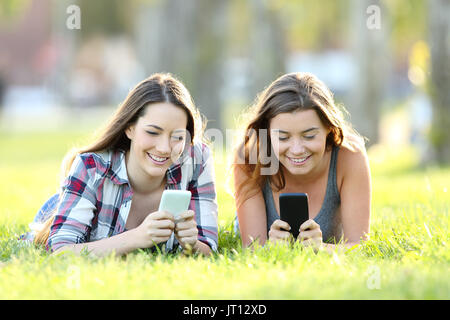 Vorderansicht des zwei glückliche Freunde über ihre Smartphones auf dem Gras in einem Park Stockfoto