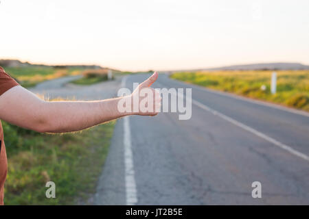 Reise, Reisen, Geste und Personen Konzept - Mann per Anhalter fahren und anhalten Auto mit Daumen nach oben Geste auf die Landschaft. Stockfoto