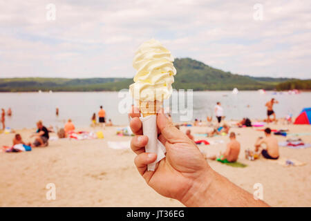 Männliche hand mit Vanilleeis bei heißem Wetter am See Strand Stockfoto