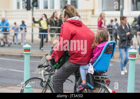 Man Radfahren mit einem Kind in einem Kindersitz ist, beide nicht das Tragen eines Helmes. Unverantwortlich Radfahrer. Stockfoto