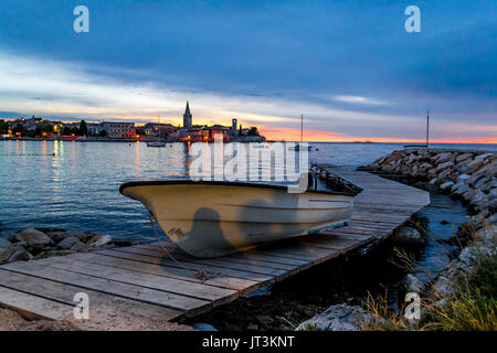 Einsames Boot auf einem Steg bei Sonnenuntergang mit einem mediterranen Altstadt im Hintergrund Stockfoto