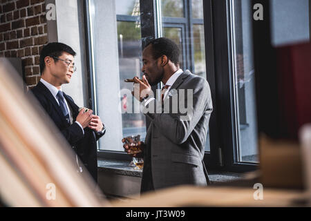 Zuversichtlich Geschäftsmann Alkohol trinken und rauchen Zigarre, während Kollege ausblenden Geld in Anzug pocket, Business Team Meeting Stockfoto