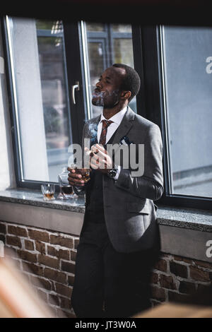 Zuversichtlich Geschäftsmann holding Glas mit Whiskey und Zigarre rauchen in Innenräumen Stockfoto