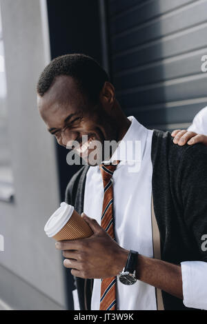 Stilvolle afrikanische amerikanische Geschäftsmann lachen und Holding Kaffee ins Freie gehen. Stockfoto