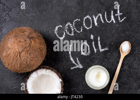 Blick von oben auf die Kokosöl in Glas Glas mit Löffel und rissig Coconut auf Schwarz Stockfoto