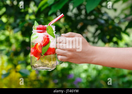 Hand, die Erdbeere Limonade mit Eis und Minze in Mason jar Outdoor. Glas Glas im Sommer erfrischende Erdbeer trinken. Kalte detox Wasser mit strawb Stockfoto