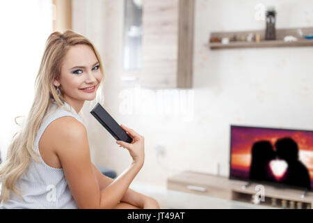 Glückliche junge Frau beobachten romantischen Film im Wohnzimmer Stockfoto