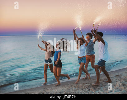 Glücklich lächelnde Freunde laufen am Strand mit funkelnden Kerzen