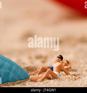 Miniatur Miniatur Mann und Frau das Tragen von Badekleidung entspannen neben einem Kunststoff blau Seesterne auf dem Sand des Strandes Stockfoto