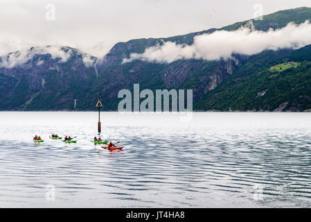 Eidfjord, Norwegen - 31. Juli 2017: Reisen Dokumentarfilm von Menschen Kajak fahren in der Gruppe im Fjord, umgeben von hohen Bergen an einem bewölkten Tag umgeben. Stockfoto