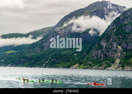 Eidfjord, Norwegen - 31. Juli 2017: Reisen Dokumentarfilm von Menschen Kajak fahren in der Gruppe im Fjord, umgeben von hohen Bergen an einem bewölkten Tag umgeben. Stockfoto