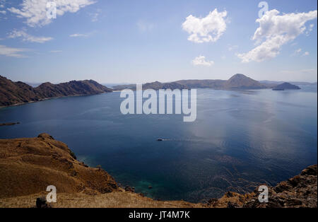 Panoramablick auf die blaue Himmel Blick auf die Hügel, Berge und das Meer mit einem kleinen Boot von der Insel Padar Teil der Komodo National Park, Flores Indonesien. Stockfoto