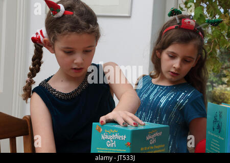 Schwestern an Weihnachten mit festlichen Alice Bands in ihren Haaren auf Sammlung von Enid Blyton Bücher das Naughtiest Girl Surrey, England Stockfoto