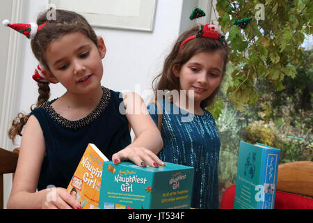 Schwestern an Weihnachten mit festlichen Alice Bands in ihren Haaren auf Sammlung von Enid Blyton Bücher das Naughtiest Girl Surrey, England Stockfoto