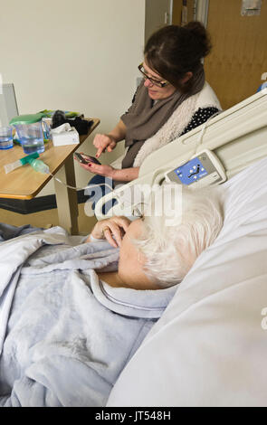 Eine ältere Dame in einem Krankenhausbett warten auf ein Care Paket, damit Ihr die Entlastung durch ein Familienmitglied besucht.. Stockfoto